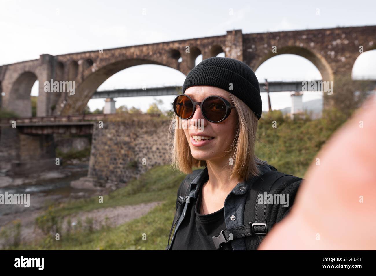 Chica blogger dirigiendo una emisión en directo del viejo puente de piedra arqueada del ferrocarril, un turista en un viaje que conduce un blog de vídeo sobre los puentes Foto de stock