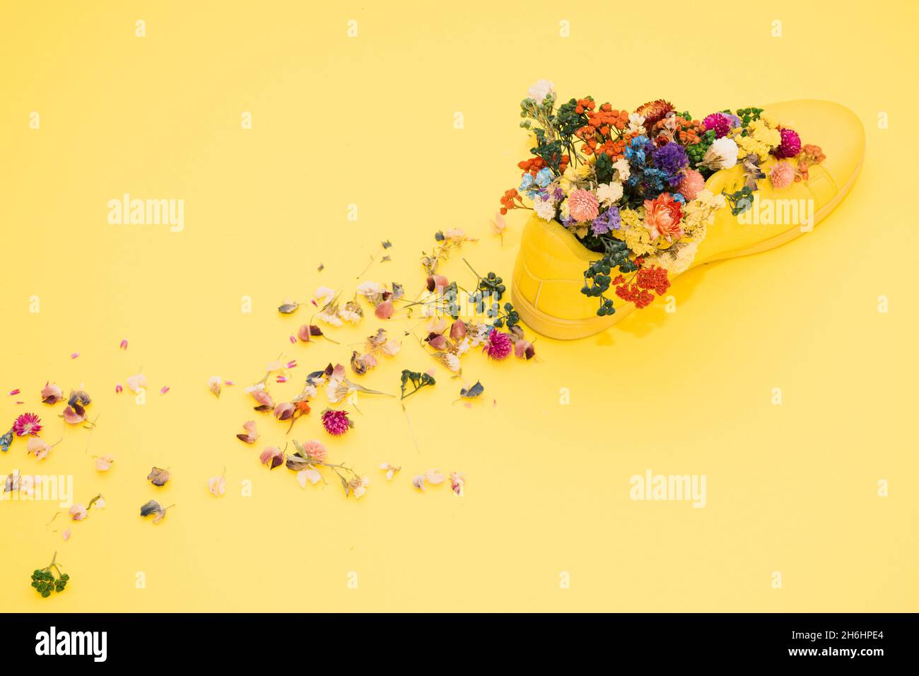 Primer plano de la bota amarilla creativa decorada con flores coloridas en la superficie amarilla Foto de stock