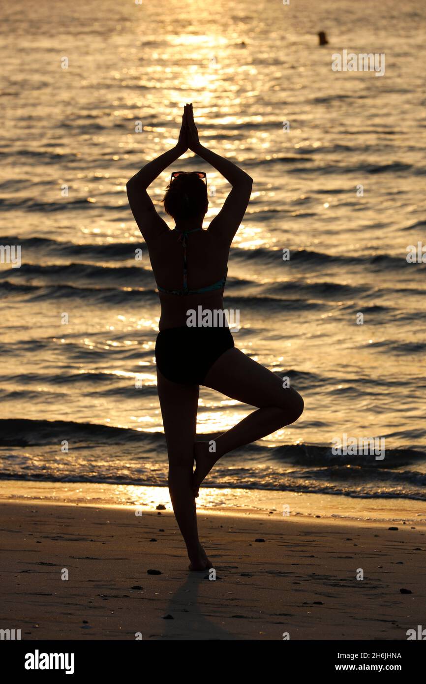 Mujer practicando yoga meditación en la playa al atardecer como concepto de silencio y relajación, Emiratos Árabes Unidos, Oriente Medio Foto de stock