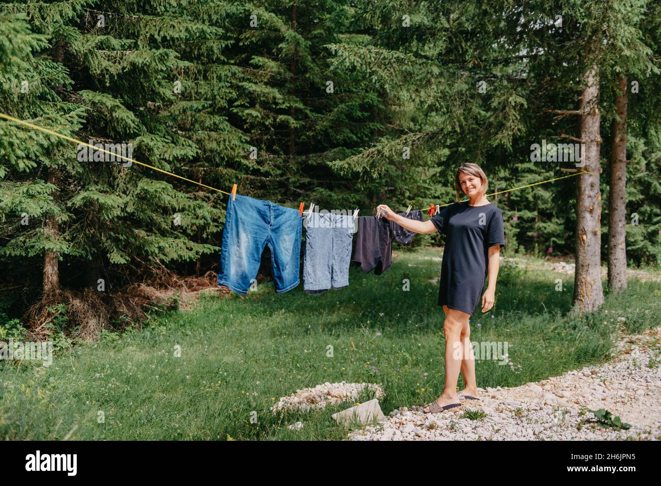 Mujer joven cuelga ropa en la línea de ropa al aire libre en el patio de  una casa de campo de pueblo, verano y concepto de frescura, día de lavado.  Chica linda