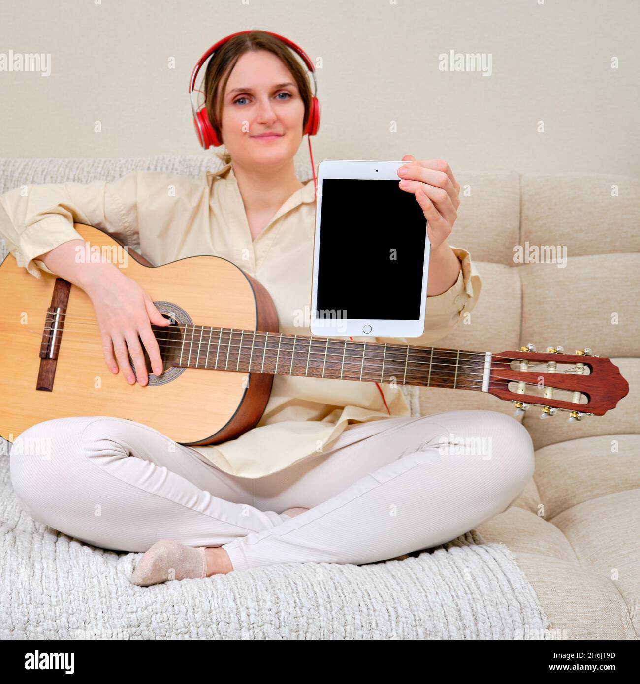 Mujer músico con una guitarra acústica sostiene una tableta Apple iPad,  burla. Guitarrista mujer sentada en una cama en un salón de casa con una  tableta disgusto Fotografía de stock - Alamy