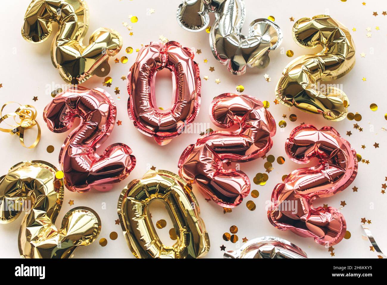 Globos multicolores hechos de papel de aluminio en forma de números 2022 con confeti sobre fondo rosa . Celebración de Navidad, Año Nuevo y concepto festivo. Plano, vista superior. Foto de stock