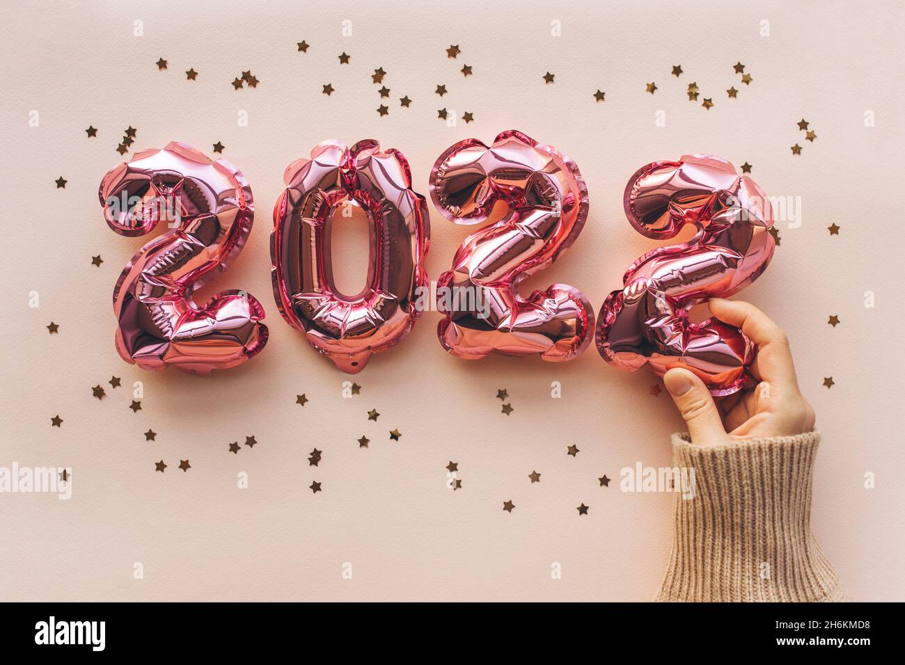 La chica presenta las figuras de Año Nuevo de 2022 sobre un fondo festivo rosa. Fondo festivo del concepto de Año Nuevo y Navidad. Plano, vista superior Foto de stock