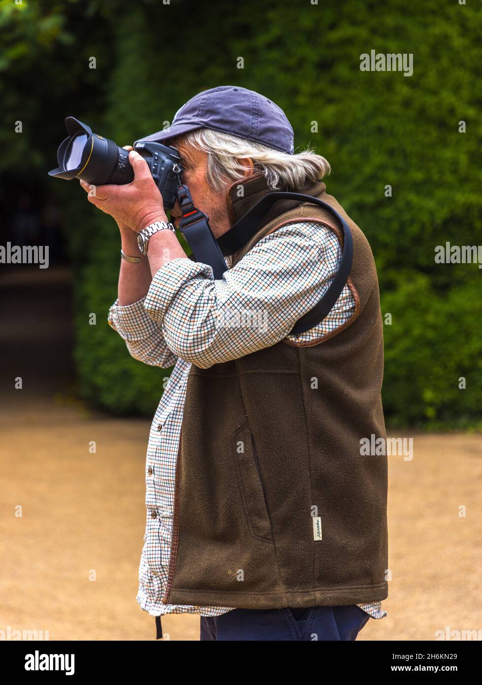 Fotógrafo masculino senior con pelo largo y con una gorra de béisbol haciendo fotos con una cámara nikon Foto de stock