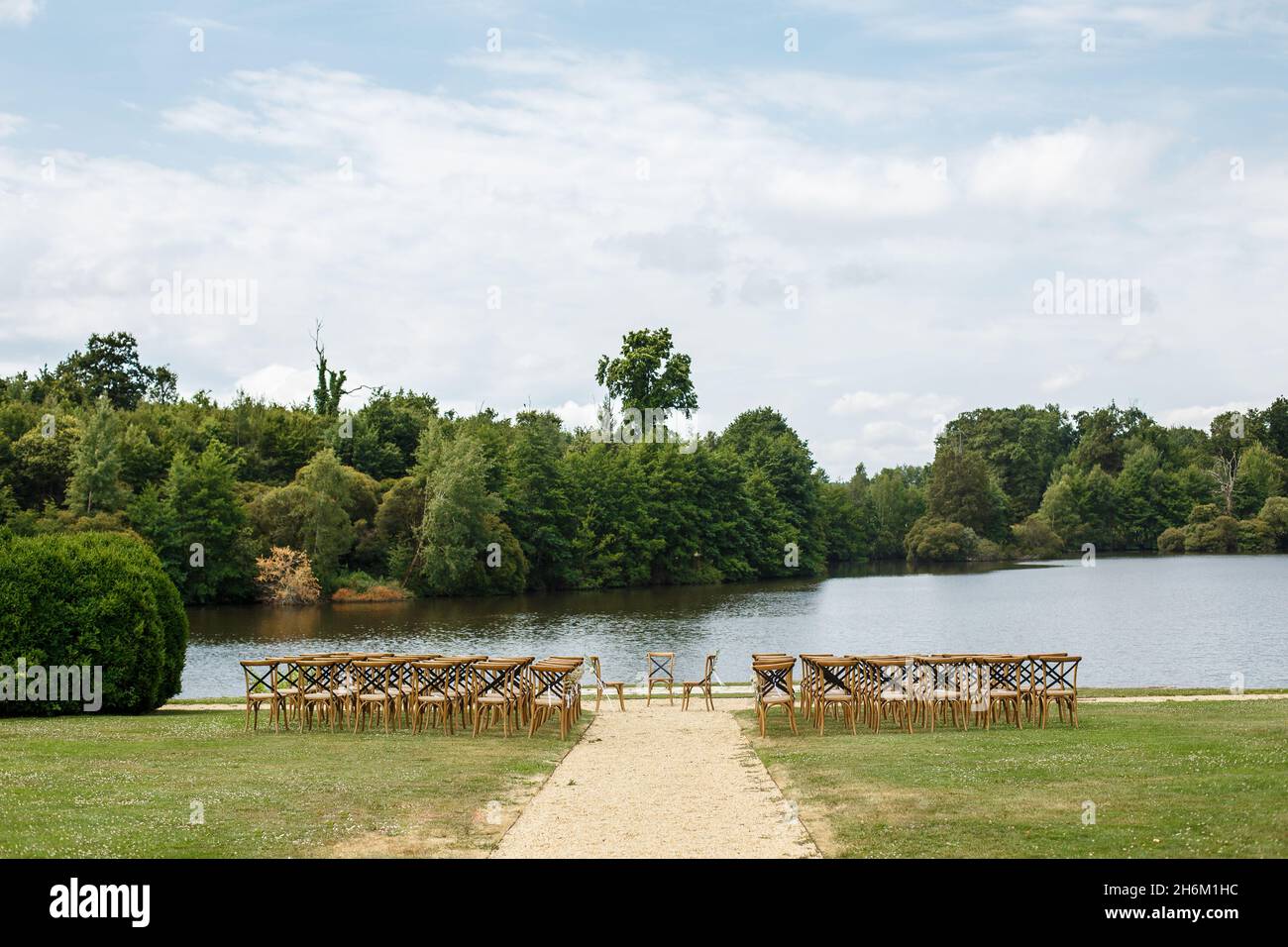 Ceremonia de boda en el fondo del lago. Filas de sillas de madera para los huéspedes de pie sobre el césped en el jardín del castillo de Francia. Foto de stock