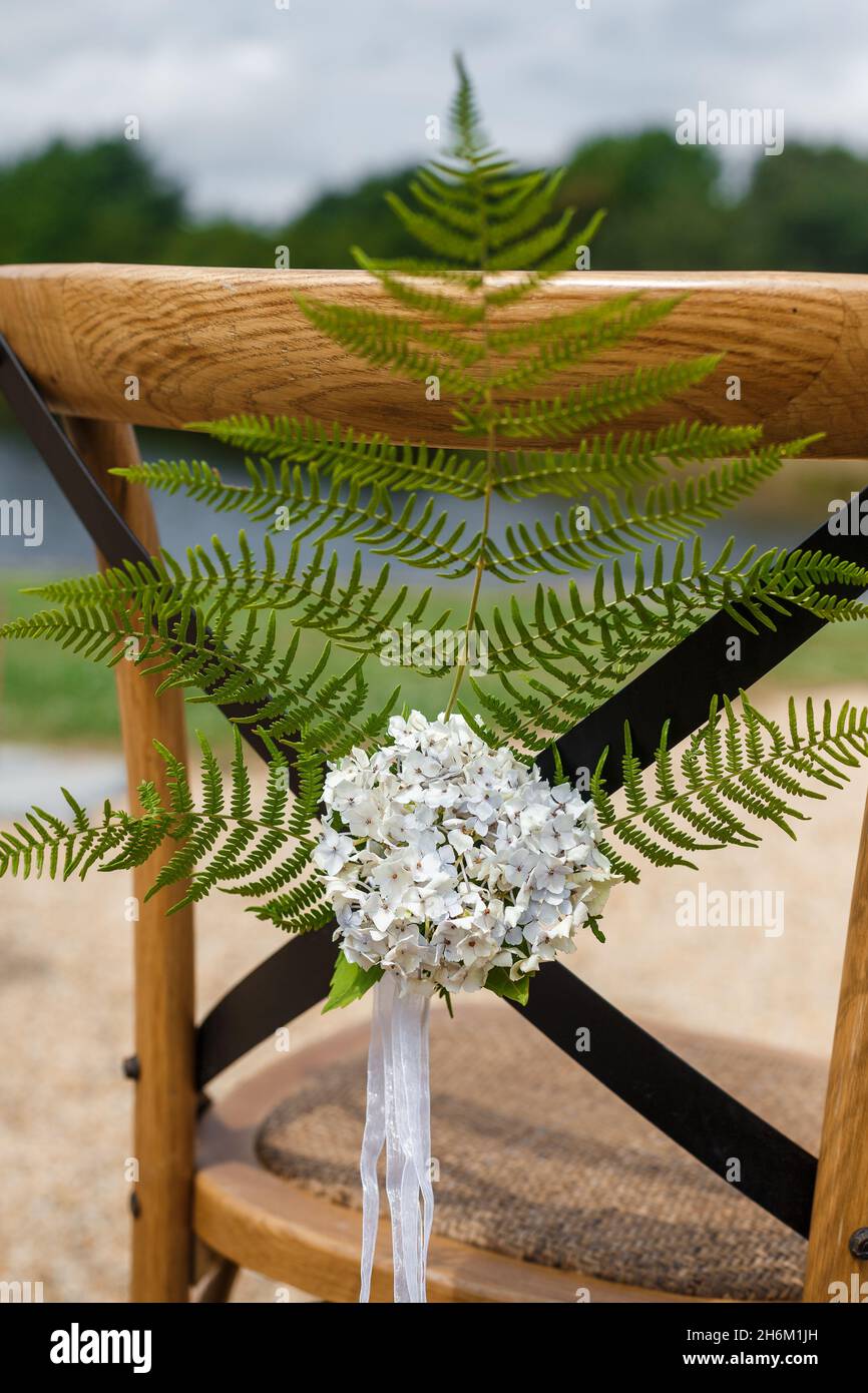 Silla de madera para huéspedes decorada con ramas de helechos, flores y cintas en estilo rústico. Decoración para ceremonias de boda Foto de stock