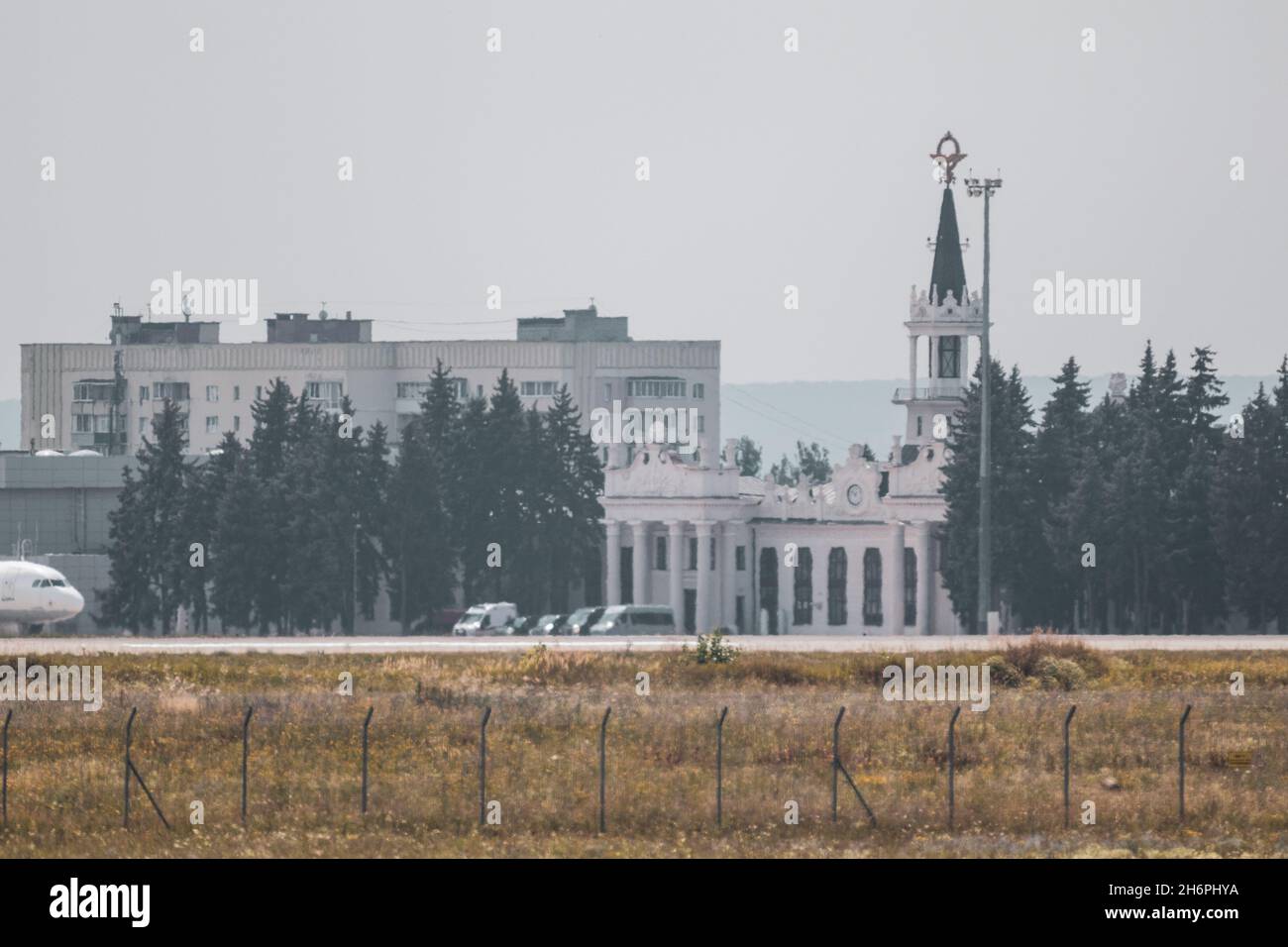 Protección del territorio del aeropuerto internacional cerca de seguridad y edificio con torre de reloj en campo de prados con vista gris cielo distante. Kharkiv, Ucrania i Foto de stock