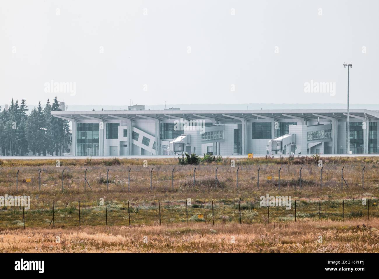 Protección del territorio del aeropuerto internacional cerca de seguridad y terminal Edificio moderno en campo de césped seco con vista gris cielo distante. Kharkiv, Ucrania Foto de stock