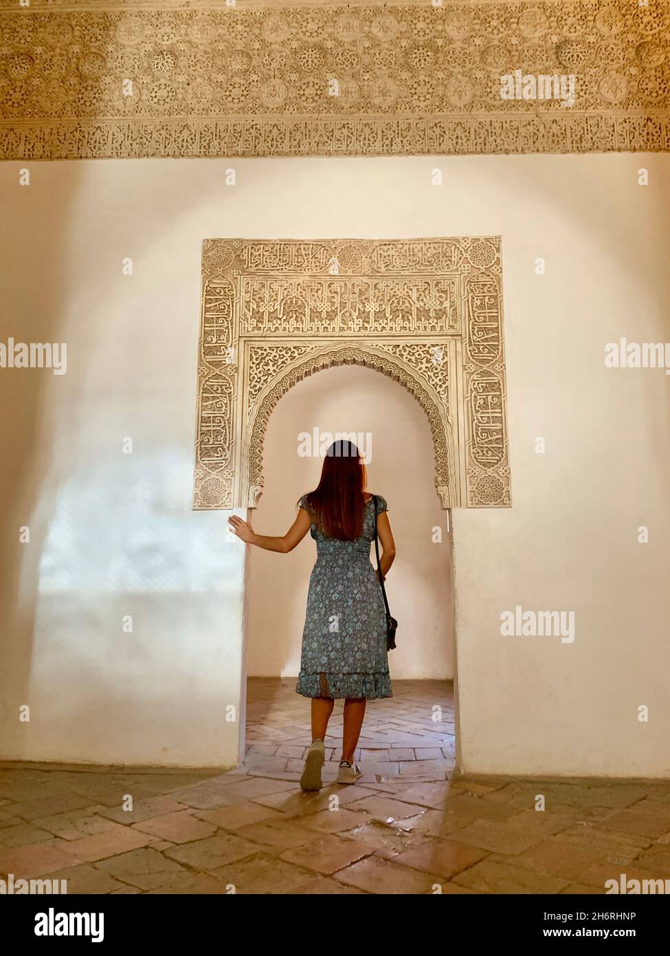 Chica morena con pelo largo caminando a través de los Palacios Nazaríes de la Alhambra en Granada, bajo una hermosa y suave luz natural creando beautifu Foto de stock