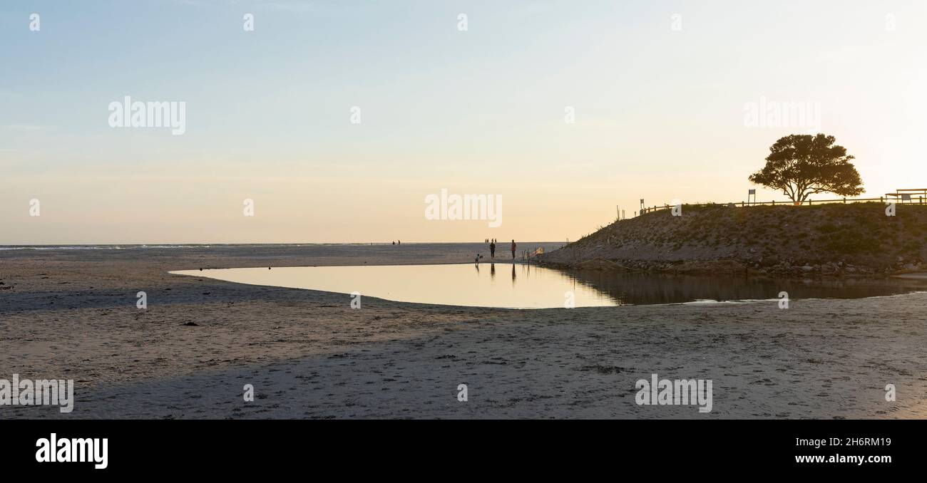 Puesta de sol, poca luz, una playa de arena abierta en marea baja, la gente en el fondo Foto de stock