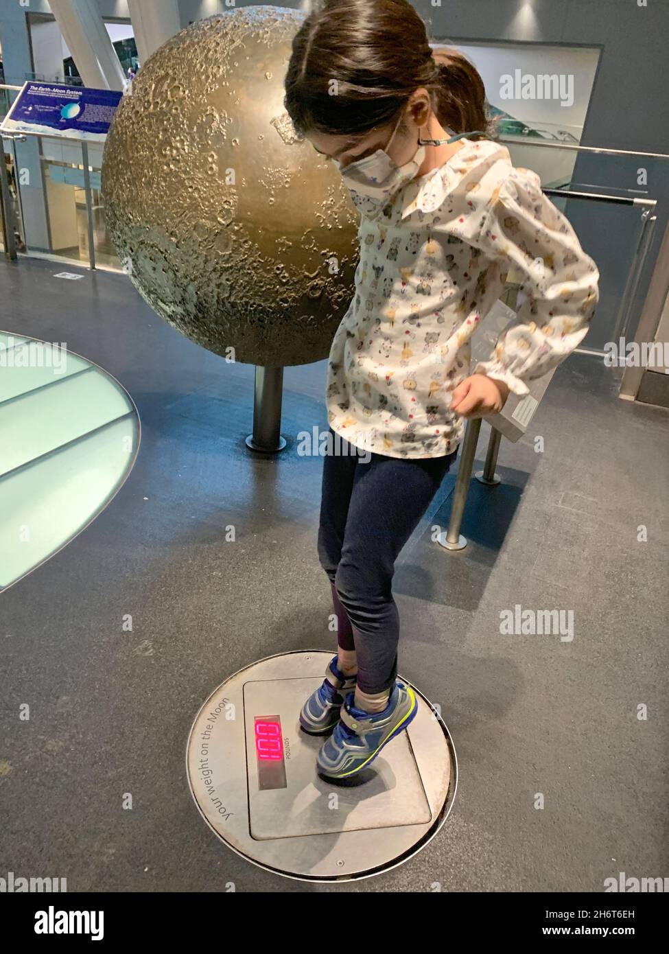 Niña, con máscara de protección, disfrutar de las exposiciones interactivas en el Centro de Rosas, y descubrir su peso en la luna. Foto de stock