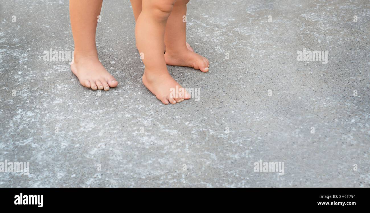 Pies de niño y bebé sobre el asfalto. El niño ayuda al menor a dar los primeros pasos. Foto de stock