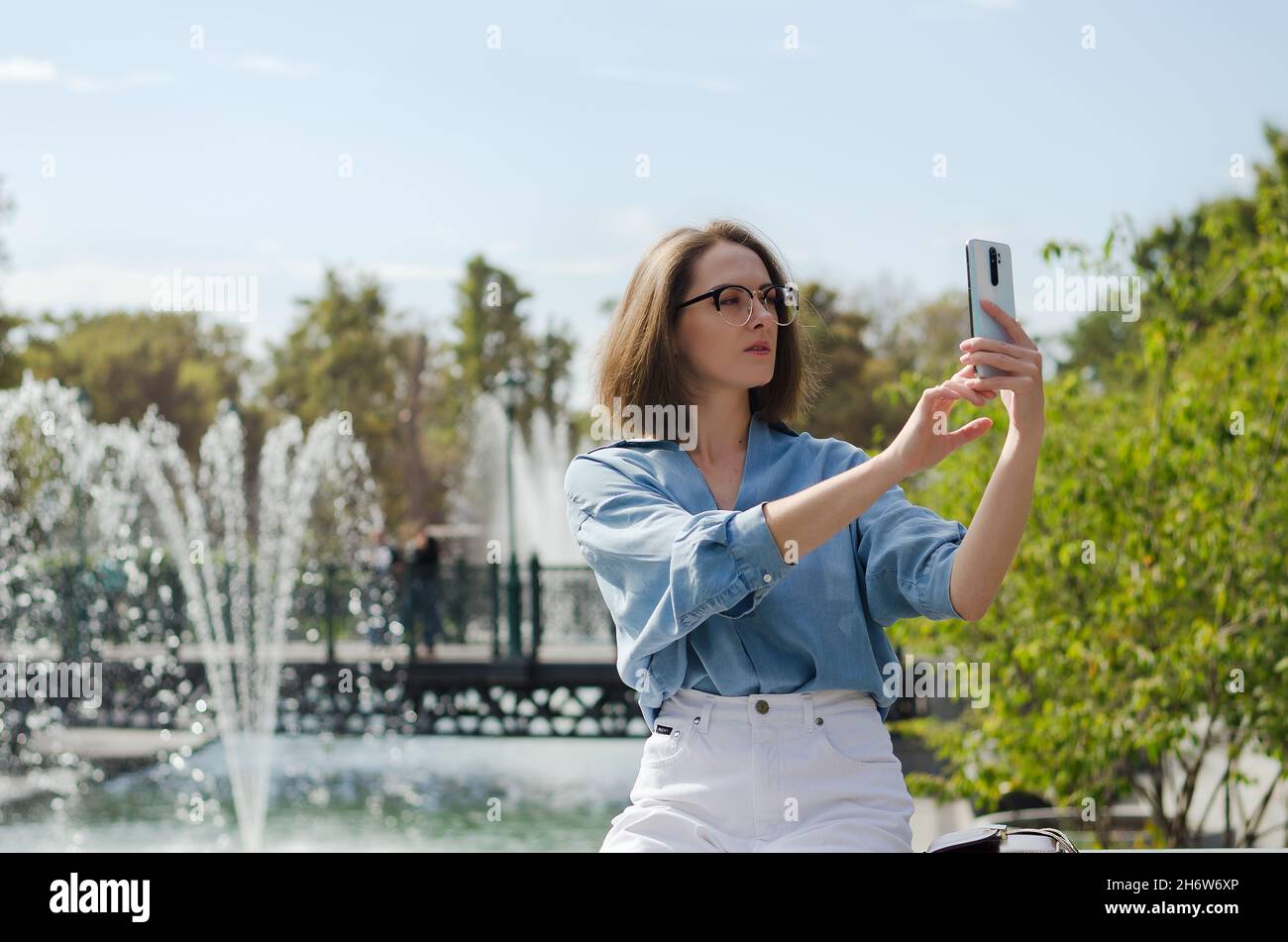 Retrato urbano de joven atractiva mujer de negocios en gafas y ropa informal. Mujer caminando en la ciudad, parque, hablando por teléfono, haciendo selfie Foto de stock