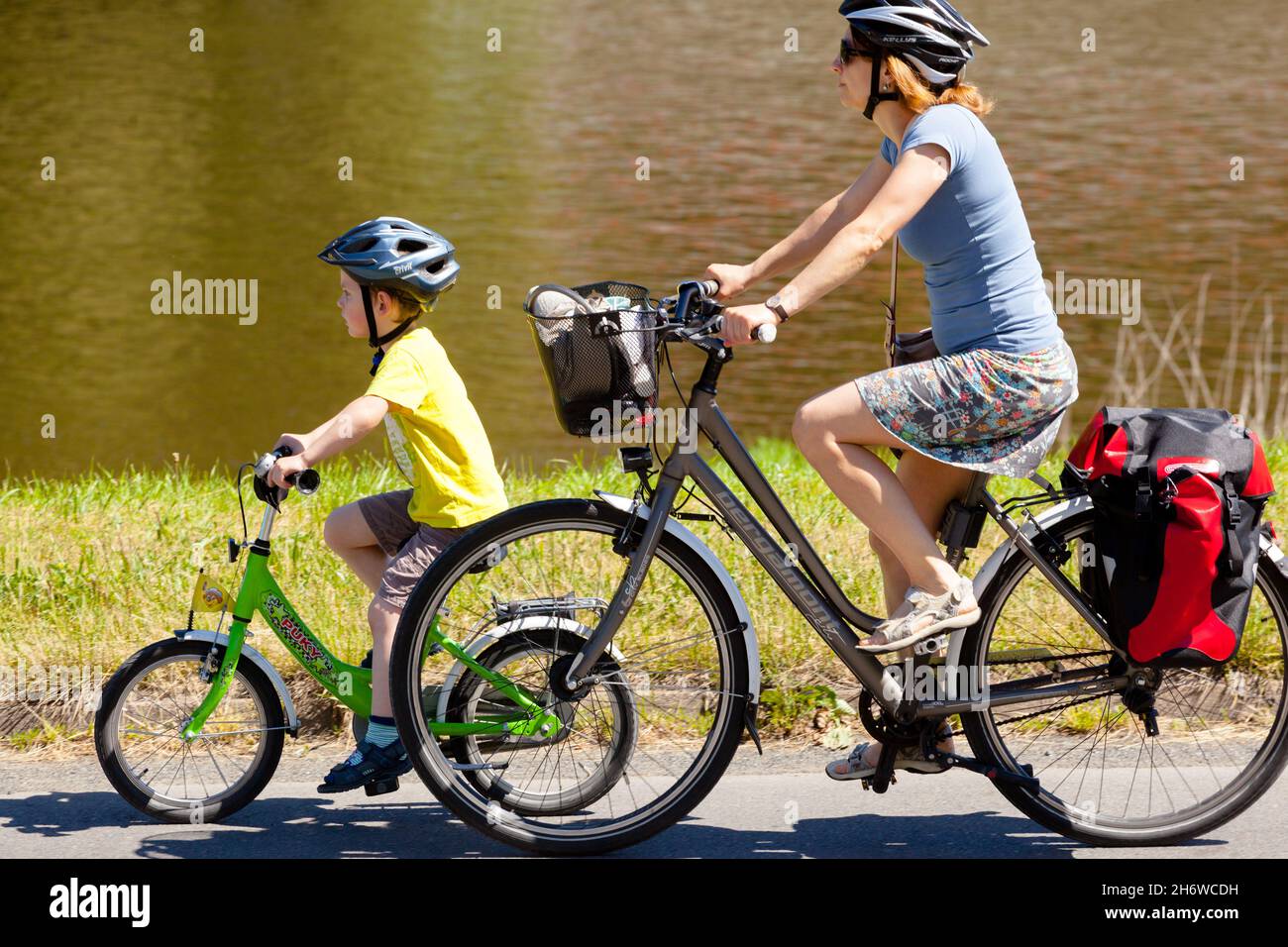 Niño montando una bicicleta con casco, niño bajo la supervisión de la madre Foto de stock