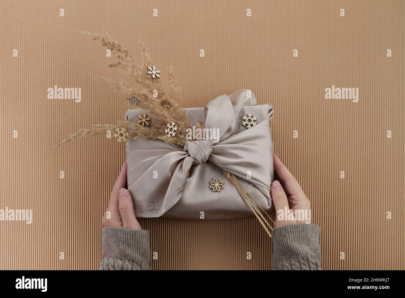Cero residuos de Navidad plana. Manos sosteniendo el regalo simple de Navidad en estilo furoshiki. Estilo de vida sostenible sin plástico Foto de stock
