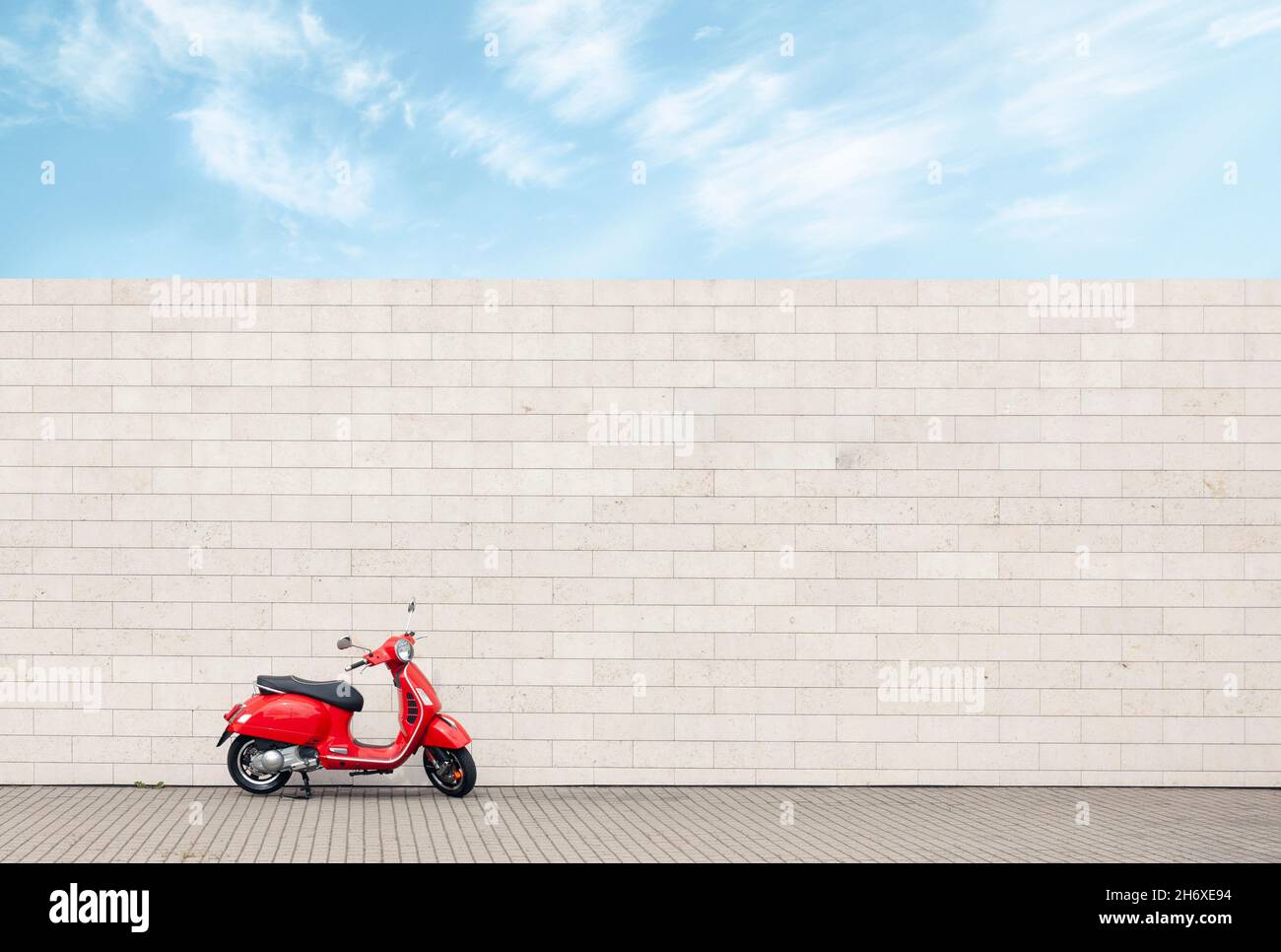 Scooter rojo solitario contra la pared blanca, minimalismo urbano con motocicleta vintage Foto de stock