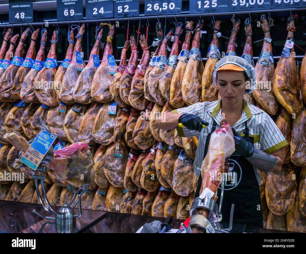 Mujer tallado jamón ibérico español con patas de jamón ahumado colgando en el supermercado, Andalucía, España Foto de stock