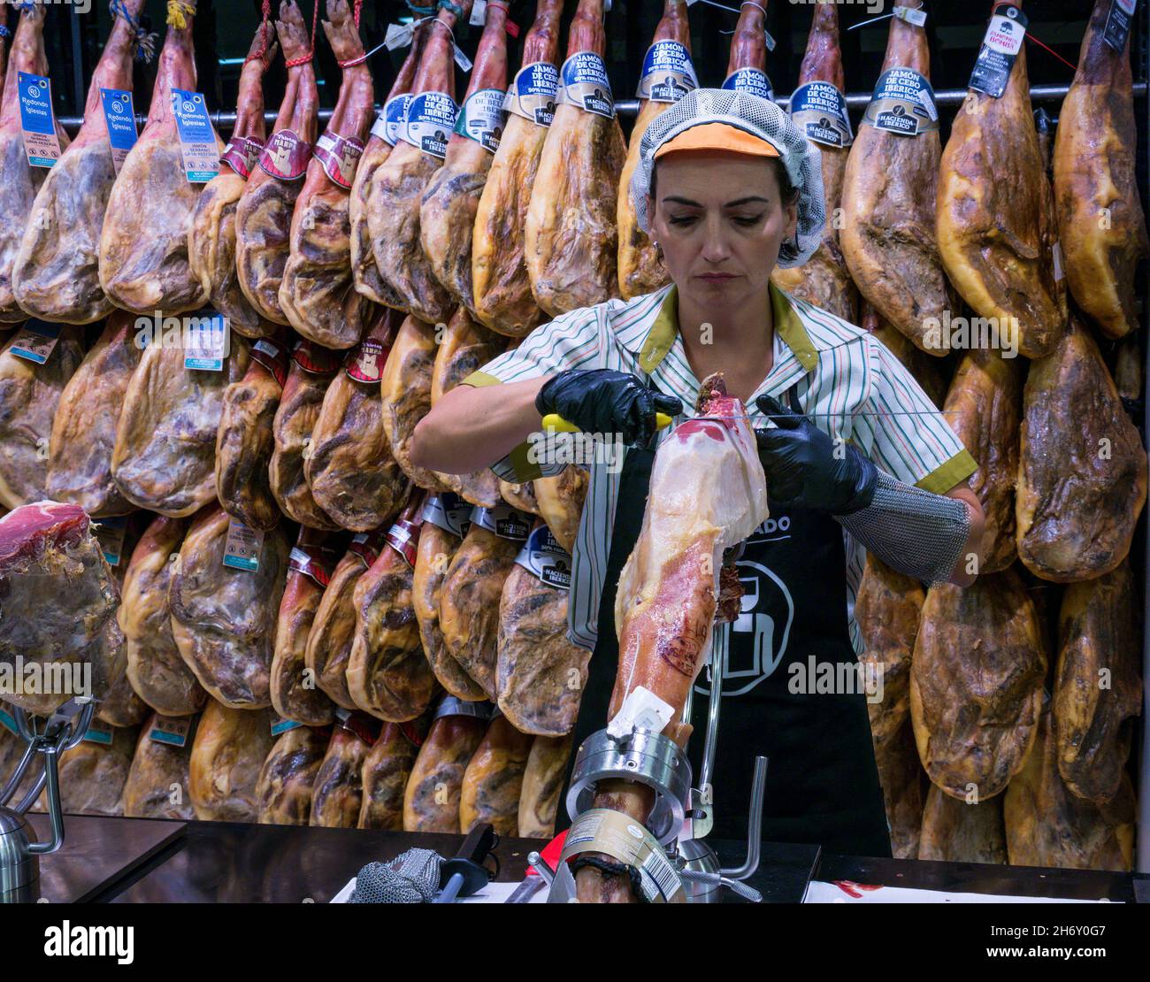 Mujer tallado jamón ibérico español con patas de jamón ahumado colgando en el supermercado, Andalucía, España Foto de stock