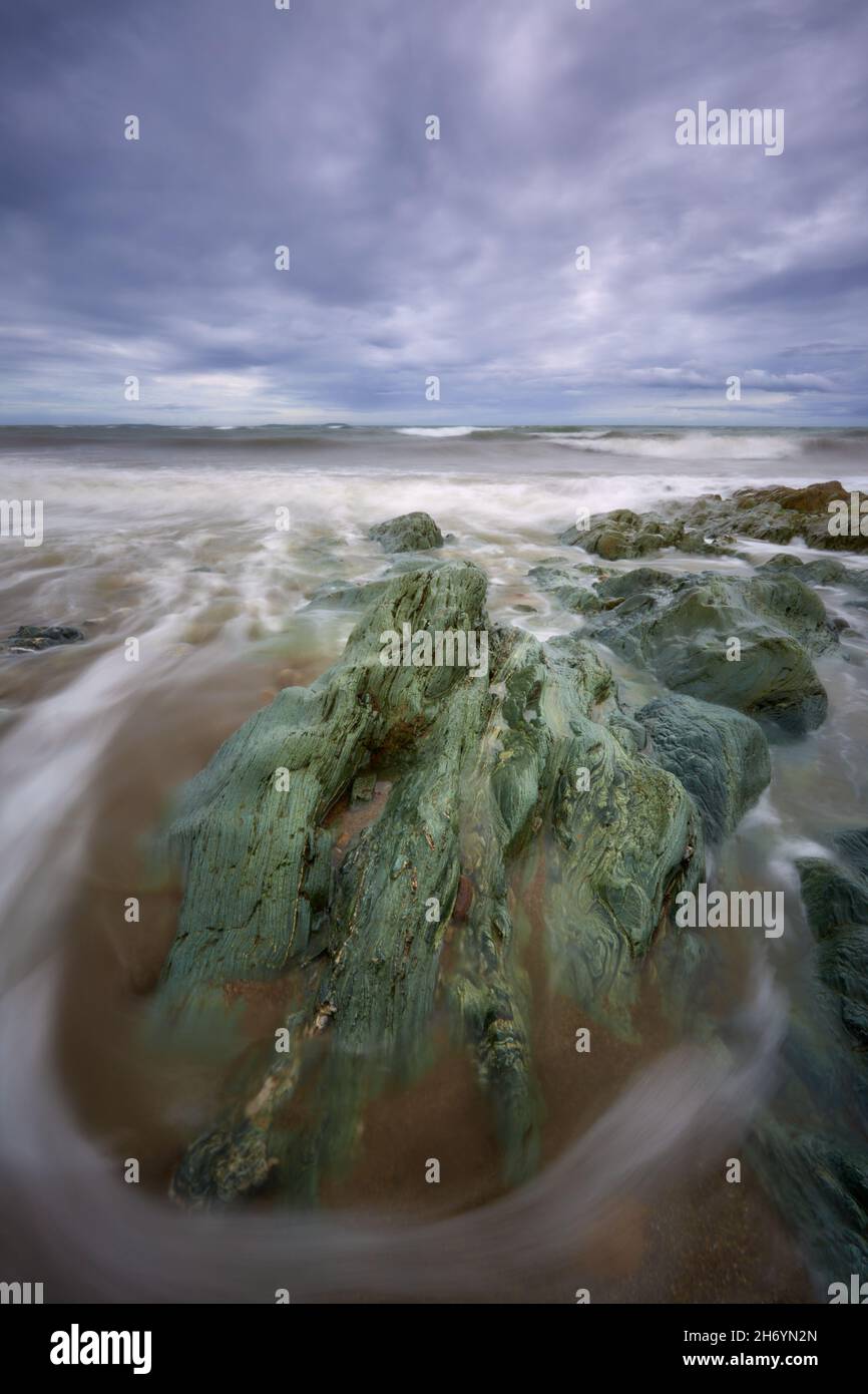 Playa de Cullenstown, Wexford, Irlanda. Espectacular primer plano lleno de rocas muy poderosas con hermosas líneas de agua que lo rodean. Muy nublado sk Foto de stock