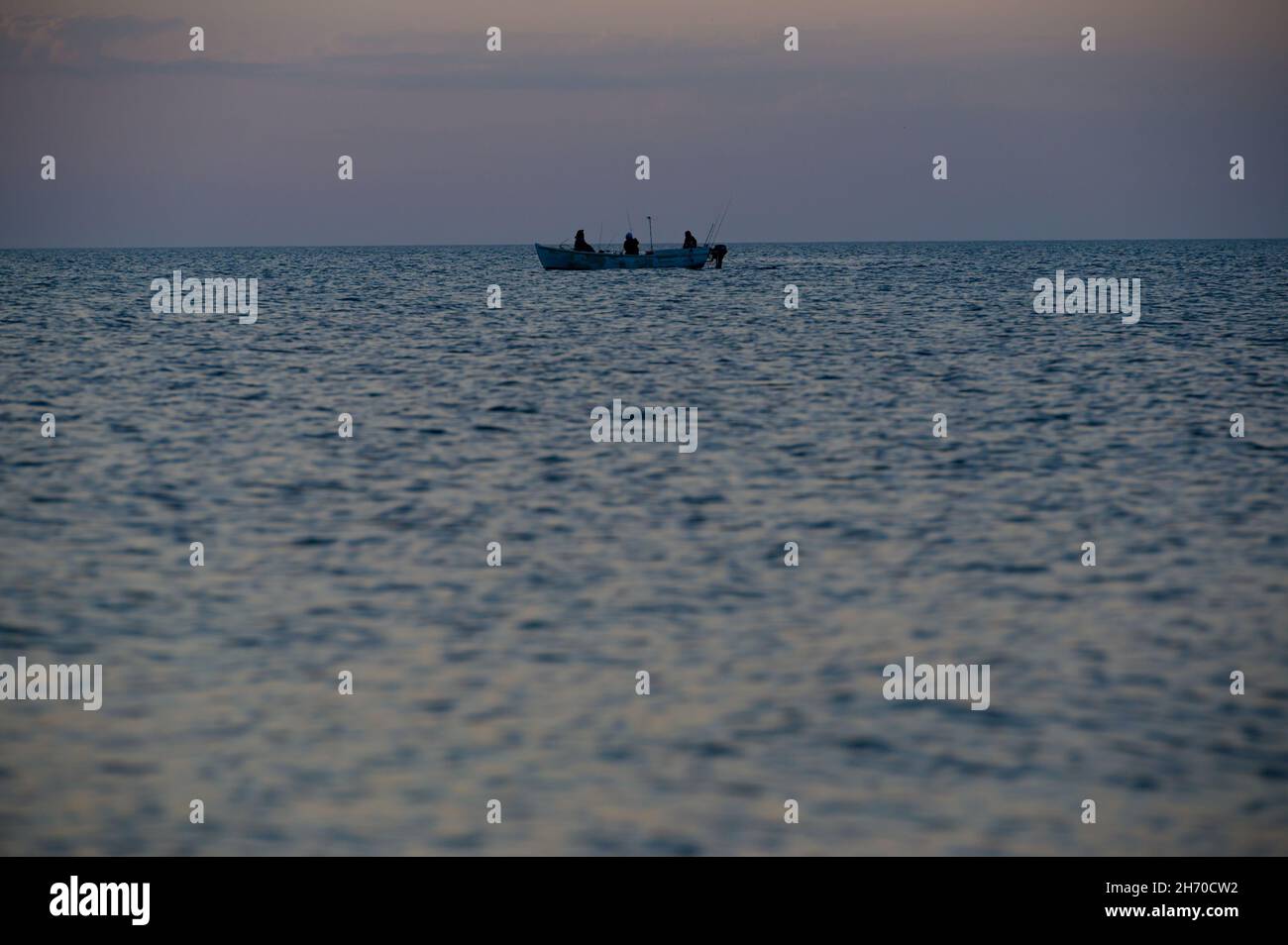 grupo de pescadores con caña en barco flotante sobre el horizonte del mar al atardecer Foto de stock