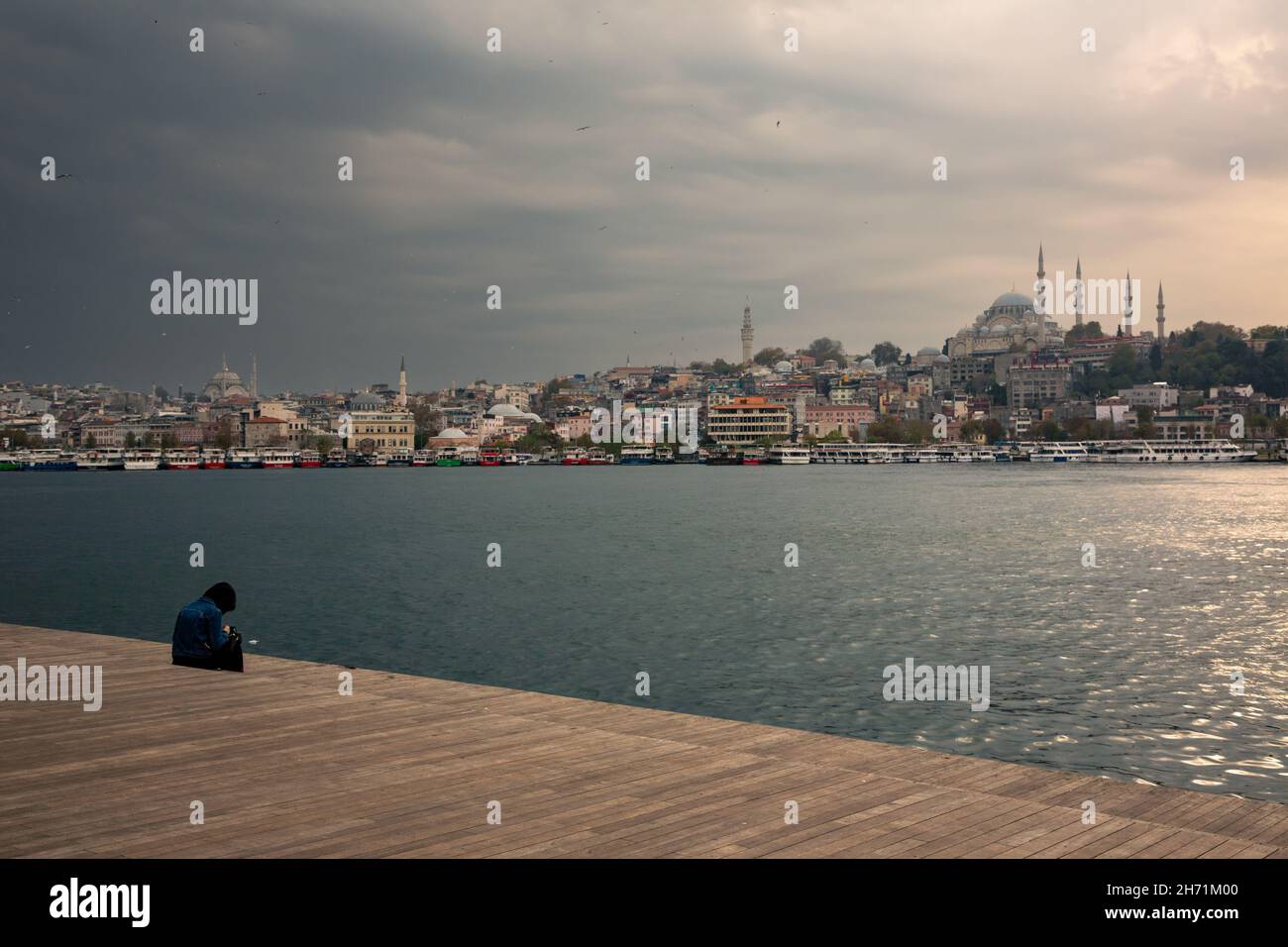 Mujer joven solitaria sentada junto al mar y viendo la puesta de sol en el Cuerno de Oro, Estambul. Foto de stock