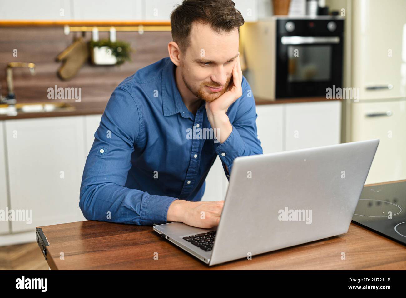 Hombre independiente centrado en la camisa elegante sport con el portátil  en la cocina en casa. Sonriente hombre trabajando de forma remota,  mensajería en línea Fotografía de stock - Alamy
