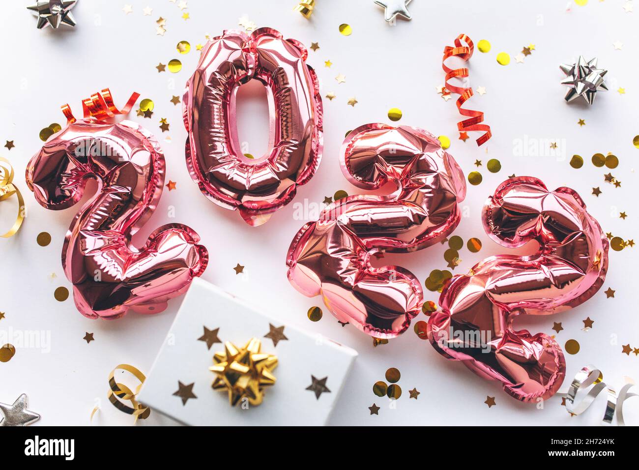 Globos de color rosa hechos de papel de aluminio en forma de números 2022 con confeti y caja de regalo sobre fondo blanco.Celebrando Navidad, Año Nuevo y el concepto festivo. Plano, vista superior. Foto de stock