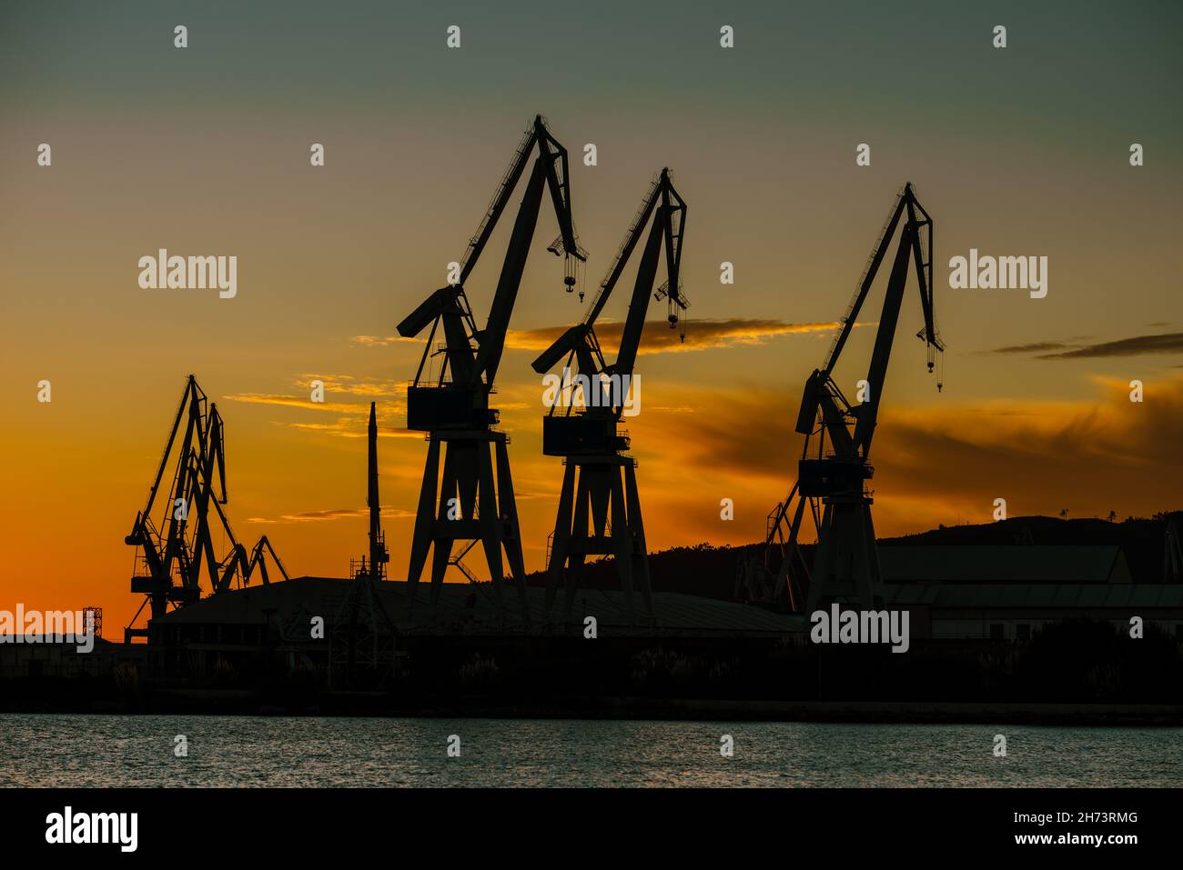 Grúas de los astilleros portuarios contra el cielo naranja Foto de stock
