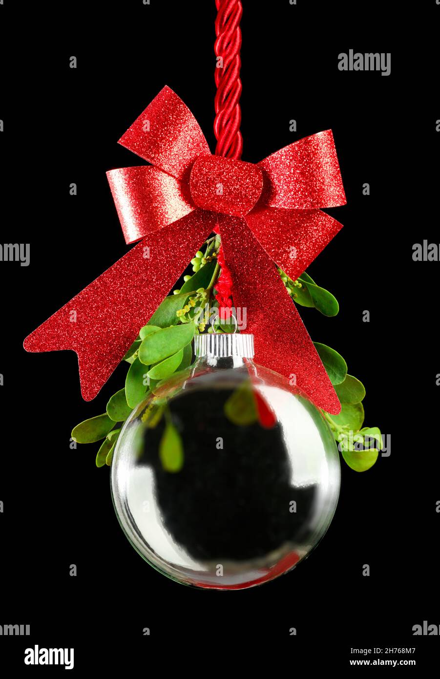 Ornamento de Navidad claro colgado por la cuerda roja de la cinta con la bola rodeada de muérdago verde. Foto de stock