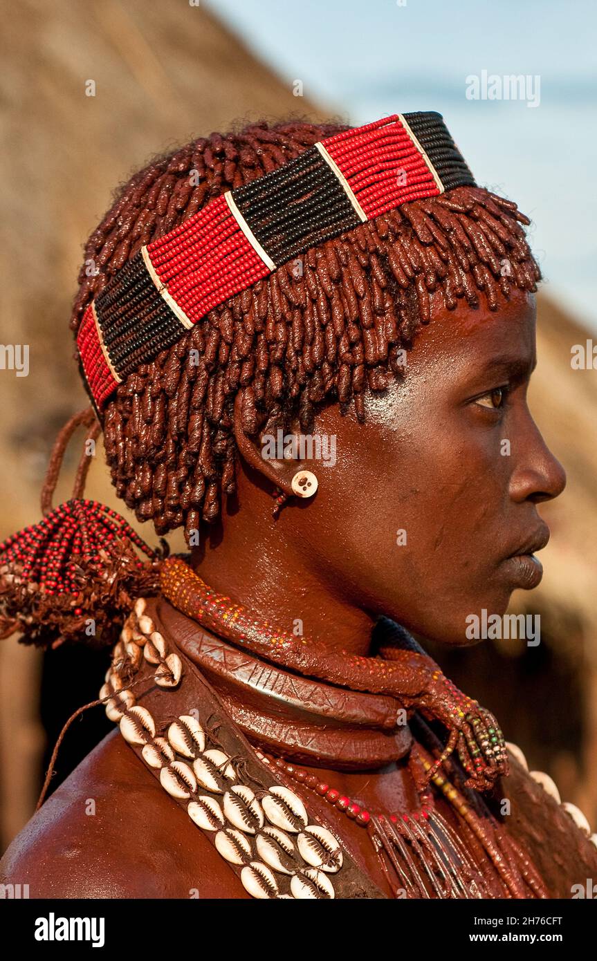 Mujer de la tribu Hamar en Etiopía con su cara y pelo cubierto de tierra de barro ocre rojo con una banda con abalorios en la cabeza Foto de stock