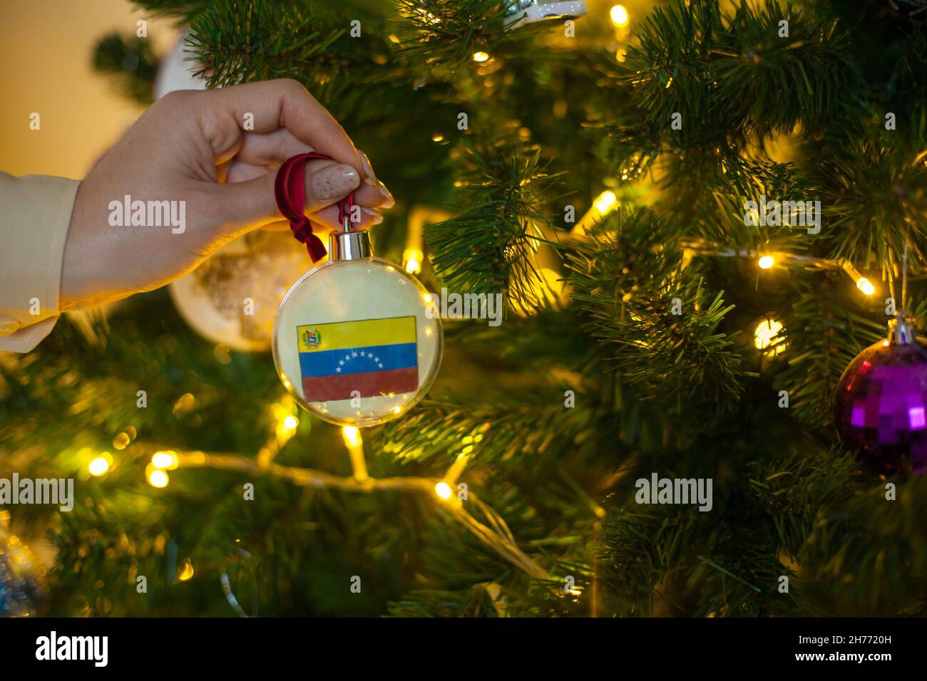 Una niña sostiene una decoración en un árbol de Navidad con la bandera de Venezuela Foto de stock