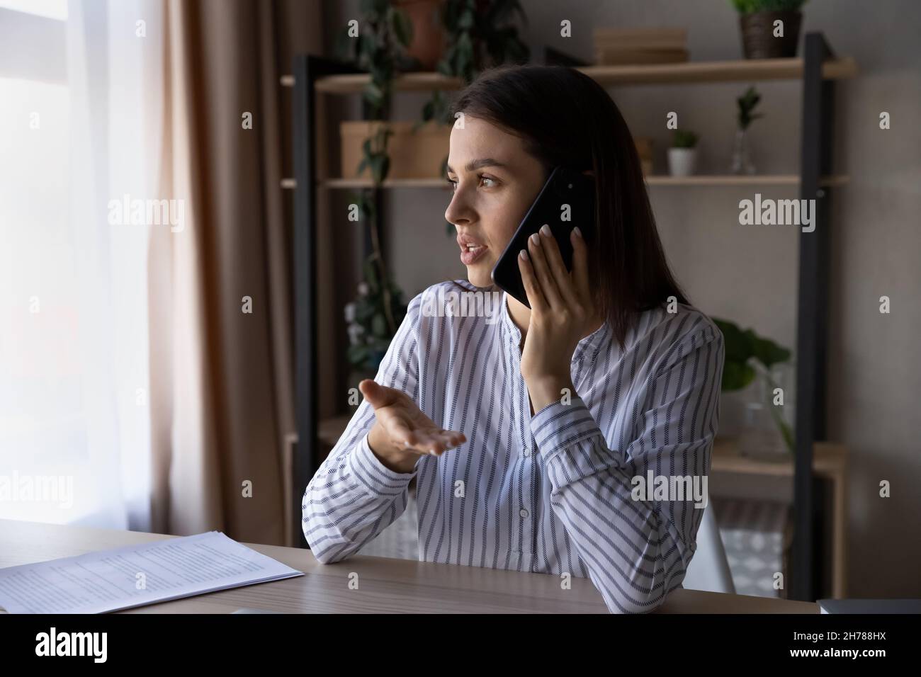 Mujer joven enfocada involucrada en la conversación de llamadas de teléfono móvil. Foto de stock