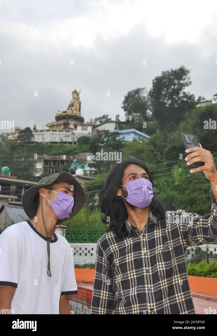 Dos amigos masculinos con máscara de la cara que lleva a selfie juntos en el exterior durante la pandemia de covid-19 Foto de stock