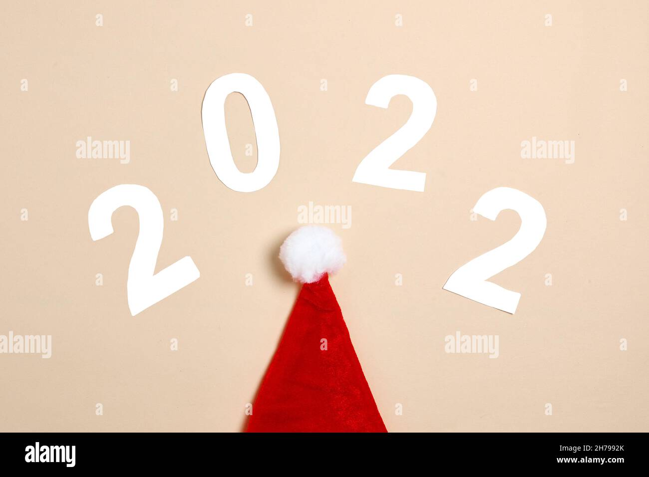 Sombrero de papá noel y 2022 números hechos de papel. Feliz Navidad y Feliz Año Nuevo concepto sobre fondo beige. 2022 fondos creativos, diseño de tarjetas Foto de stock