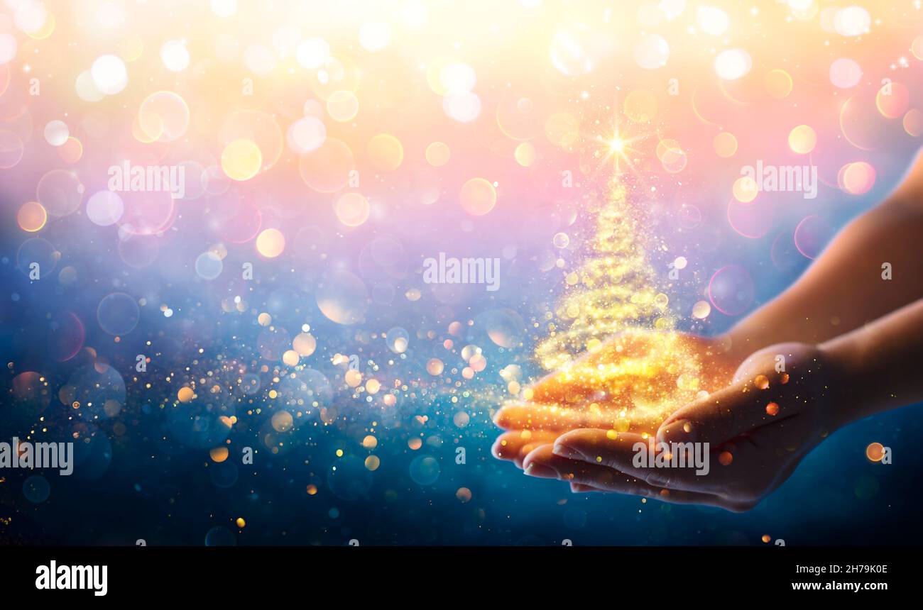 Árbol de Navidad Mágico - Luz de oro brillante en manos por la noche Foto de stock