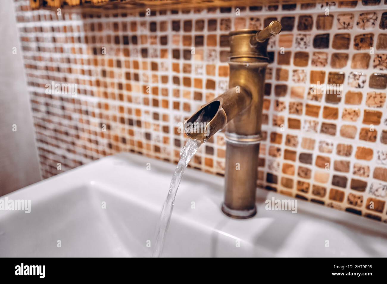 Un grifo de cobre creativo inusual en el cuarto de baño desde el que fluye una corriente de agua. El concepto de reparación y agua potable limpia Foto de stock