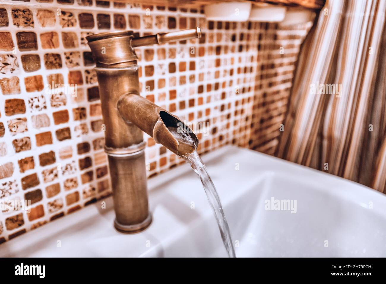 Un grifo de cobre creativo inusual en el cuarto de baño desde el que fluye una corriente de agua. El concepto de reparación y agua potable limpia Foto de stock