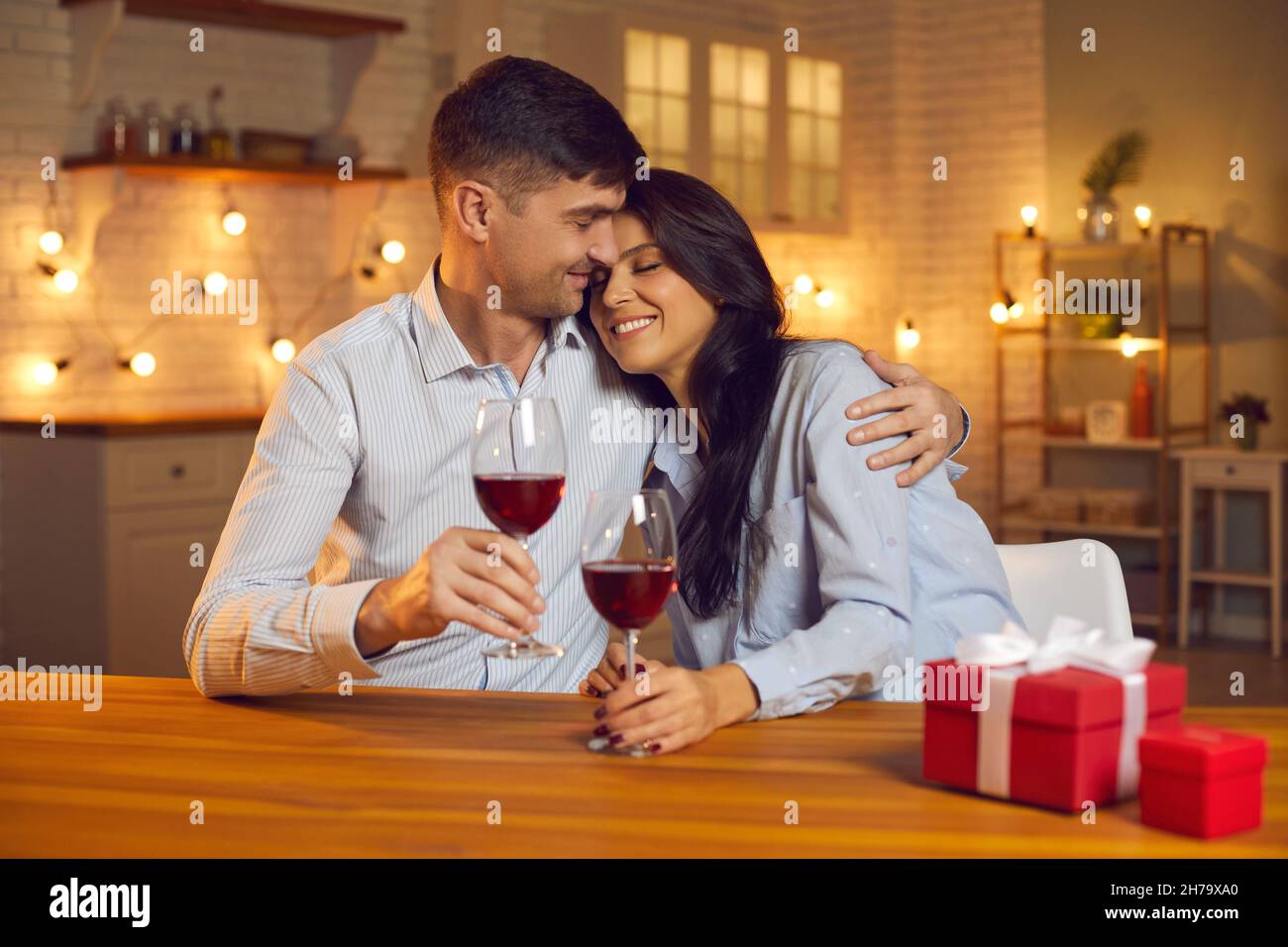 Feliz pareja cariñosa abrazando, deinando vino, dando regalos de vacaciones y celebrando el día de San Valentín Foto de stock