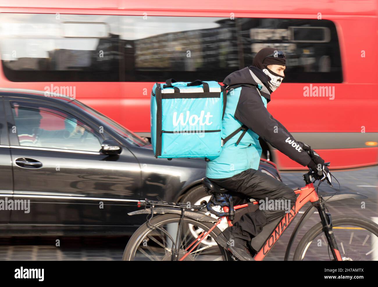 Belgrado, Serbia - 17 de noviembre de 2021: Un joven que trabaja para el servicio de entrega de alimentos de la ciudad de Wolt en bicicleta por la ajetreada calle de la ciudad Foto de stock