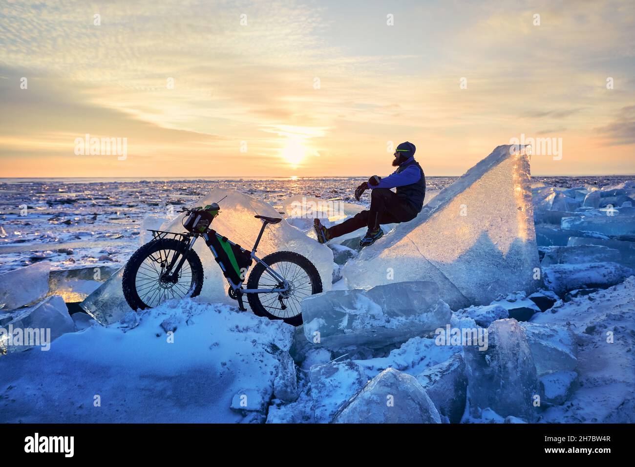 Hombre con bicicleta gorda en el lago congelado Kapchagay al atardecer en Kazajstán Foto de stock