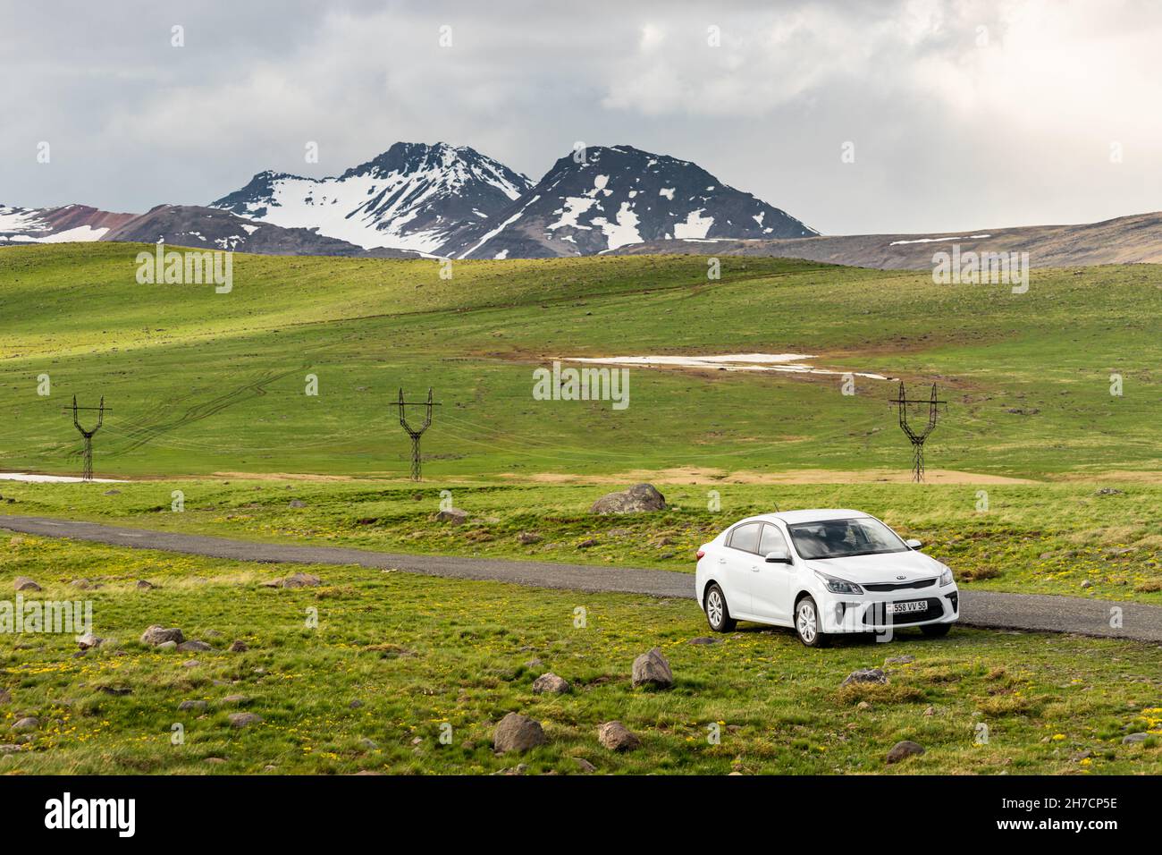 19 de mayo de 2021, Aragats, Armenia: El coche blanco de kia río está estacionado por una carretera estrecha que conduce al Monte Aragats entre prados pintorescos a principios de la primavera Foto de stock