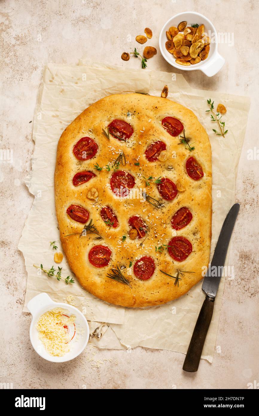 Pan italiano tradicional focaccia horneado con tomates cherry, parmesano y romero sobre fondo marrón claro. Vista superior Foto de stock