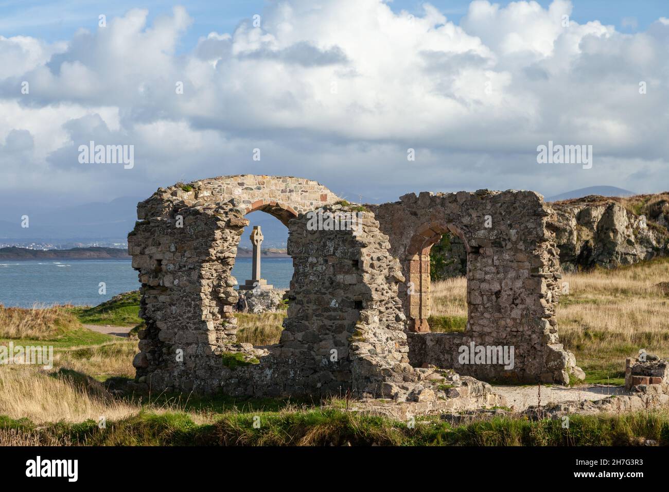 La cruz celta vio a través de las ruinas de la iglesia de San Dwynwen en la isla de Llanddwyn, Anglesey, Gales Foto de stock