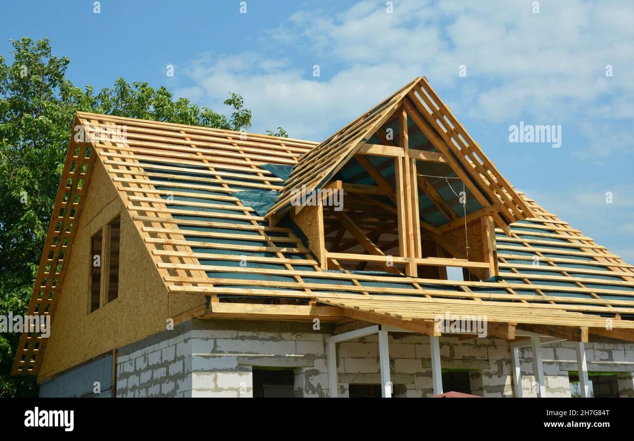 Construcción y enmarcado de tejados a dos aguas. Una construcción  incompleta de la casa del bloque del hormigón con el enmarcar del techo de  madera instalado sobre la membrana verde del vapor