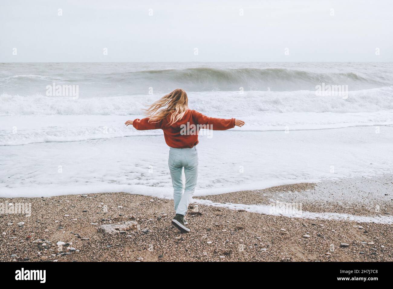 Mujer gozando de mar tormentoso corriendo en la playa felices manos elevadas saludable estilo de vida aventura vacaciones al aire libre Foto de stock