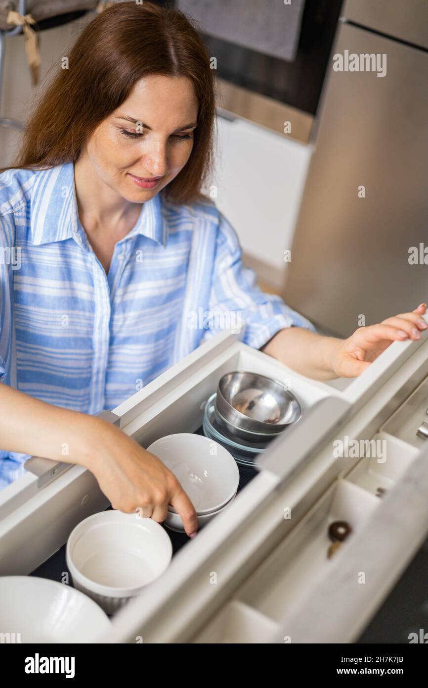 Ama de casa moderna ordenando el armario de la cocina durante la limpieza  general o el ordenamiento