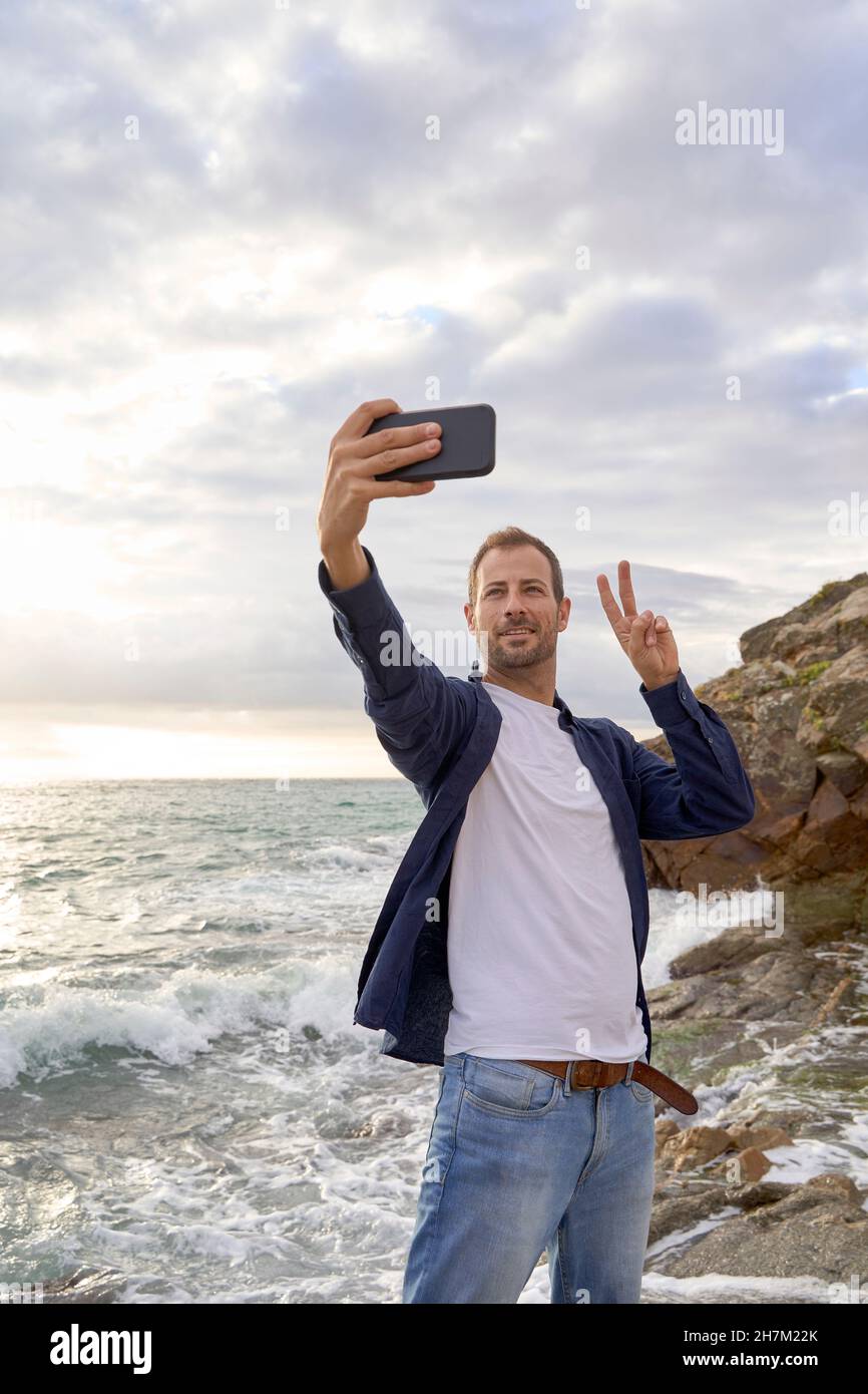 Hombre mostrando señal de paz tomando selfie en la playa Foto de stock