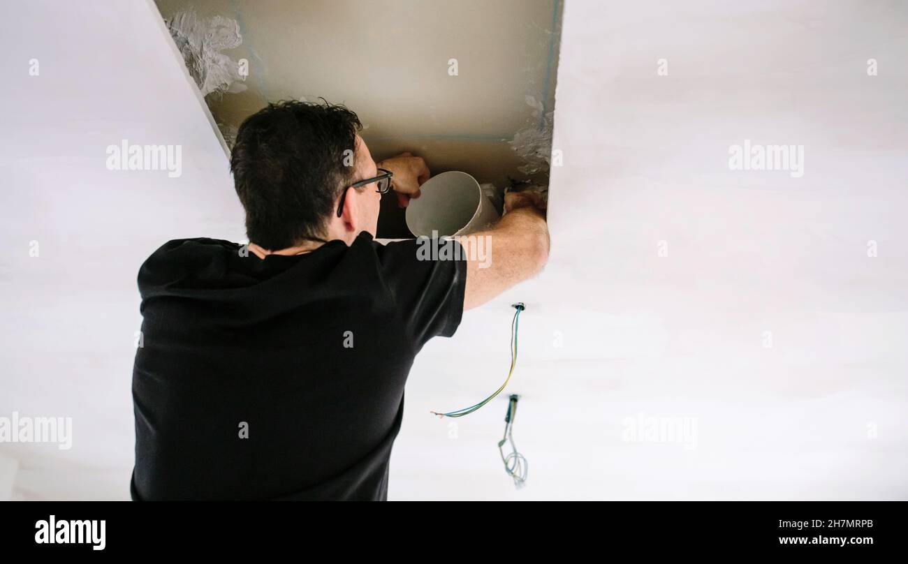 Hombre colocando el tubo para la instalación de la campana de cocina en el techo de la cocina Foto de stock
