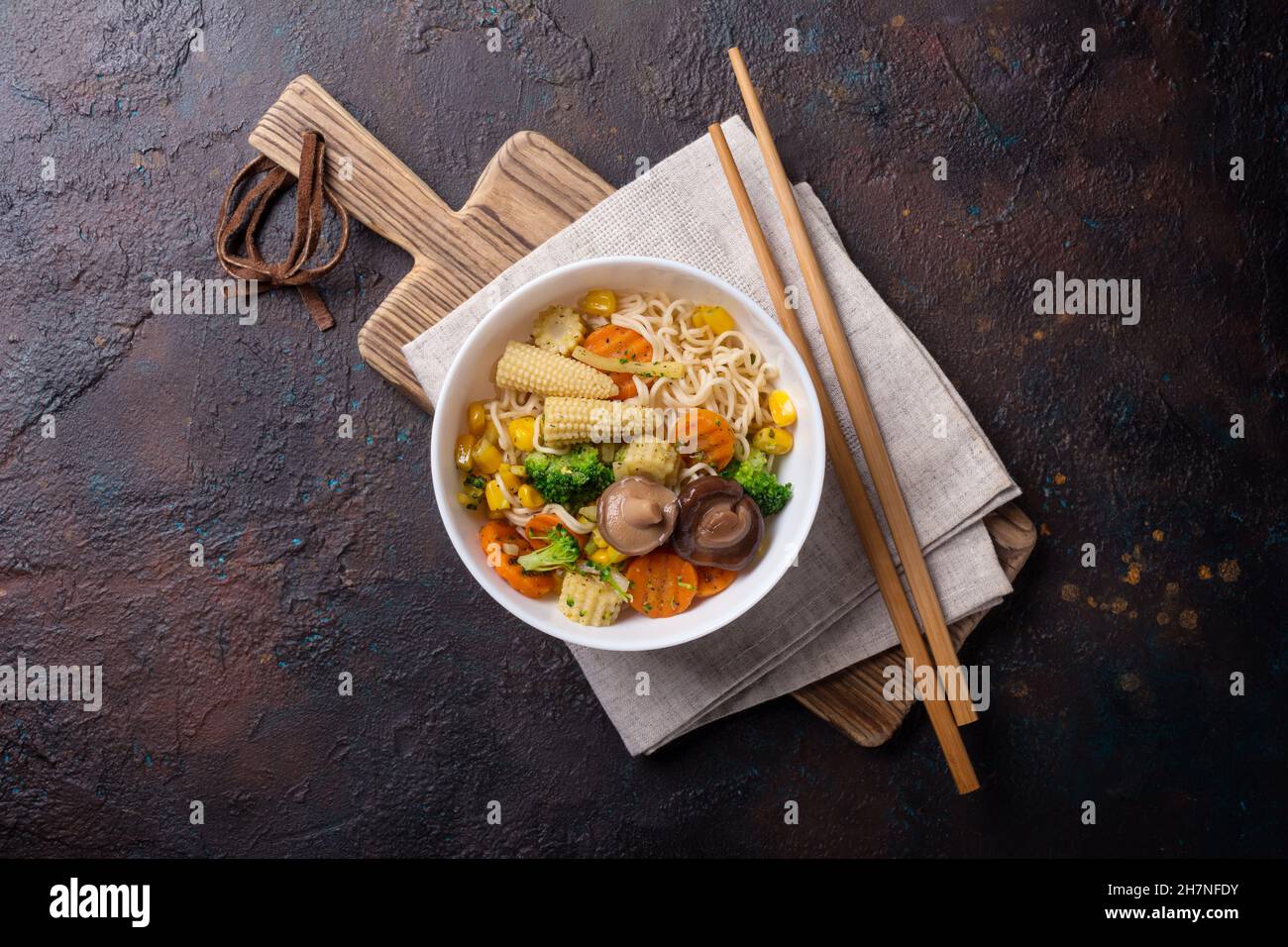 Vista superior del plato con fideos asiáticos, maíz, brócoli, zanahoria y setas shiitake sobre fondo de hormigón oscuro Foto de stock
