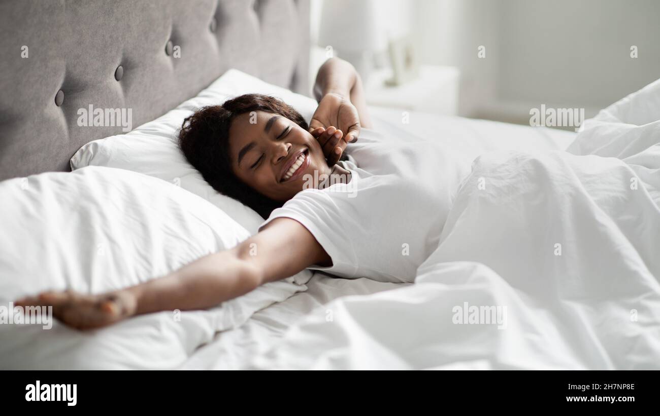 Mujer negra joven disfrutando de la mañana feliz en la cama Foto de stock